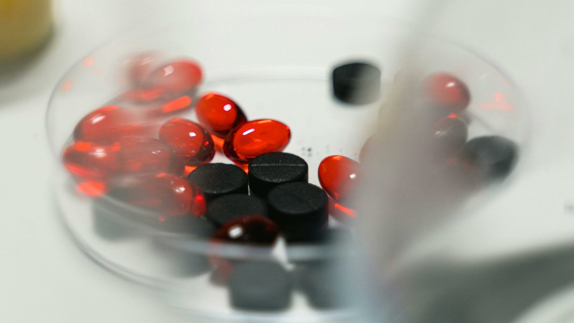 Red and black pills in a petri dish, ideal for healthcare and pharmaceutical themes.